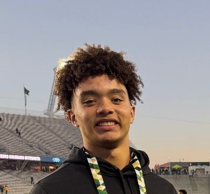 Young person smiling in a stadium with empty stands and flags in the background.