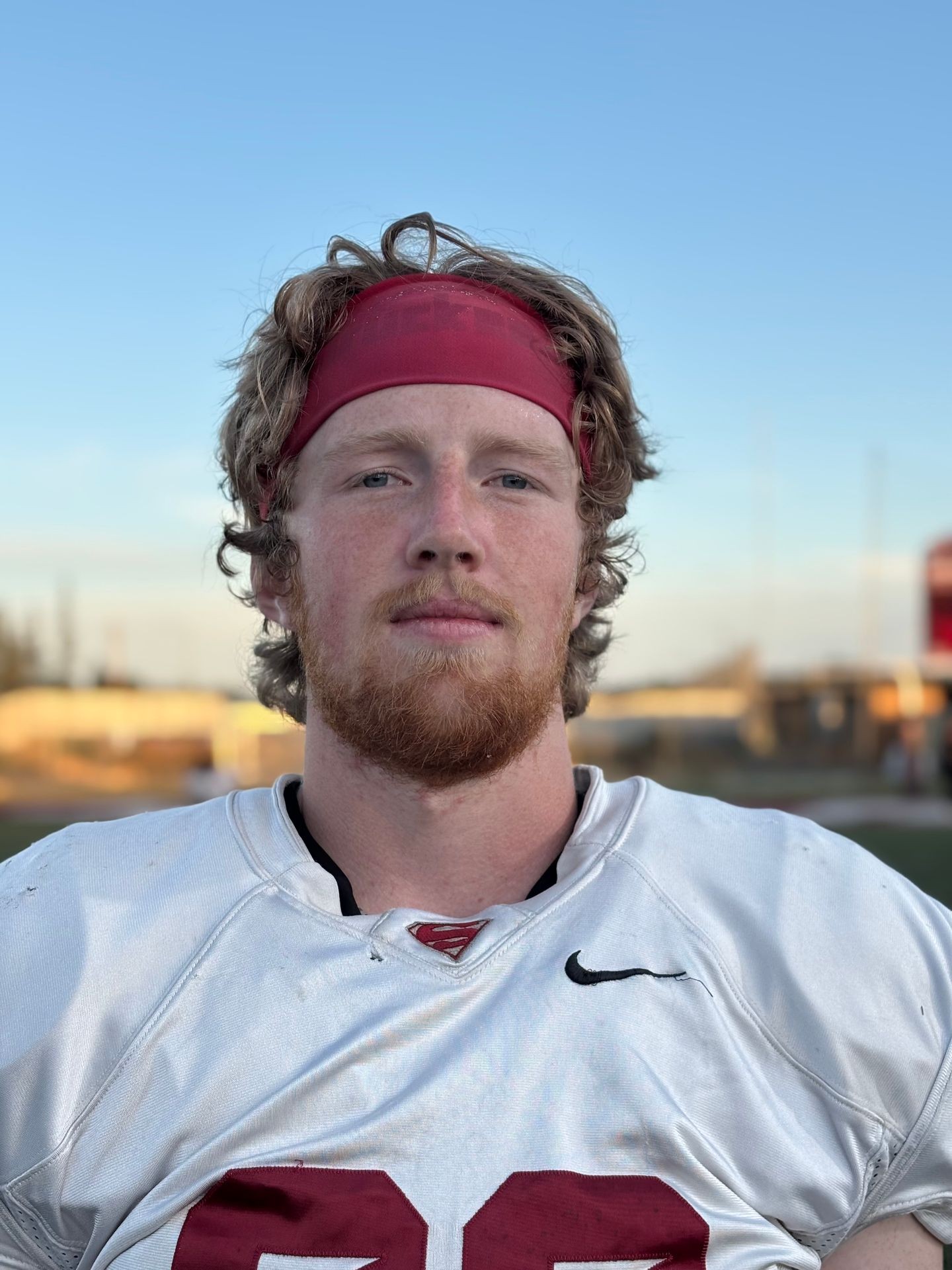 Football player with red headband and white jersey standing on field under clear blue sky.