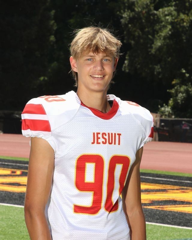 A football player in a Jesuit jersey with number 90 smiling on a field.